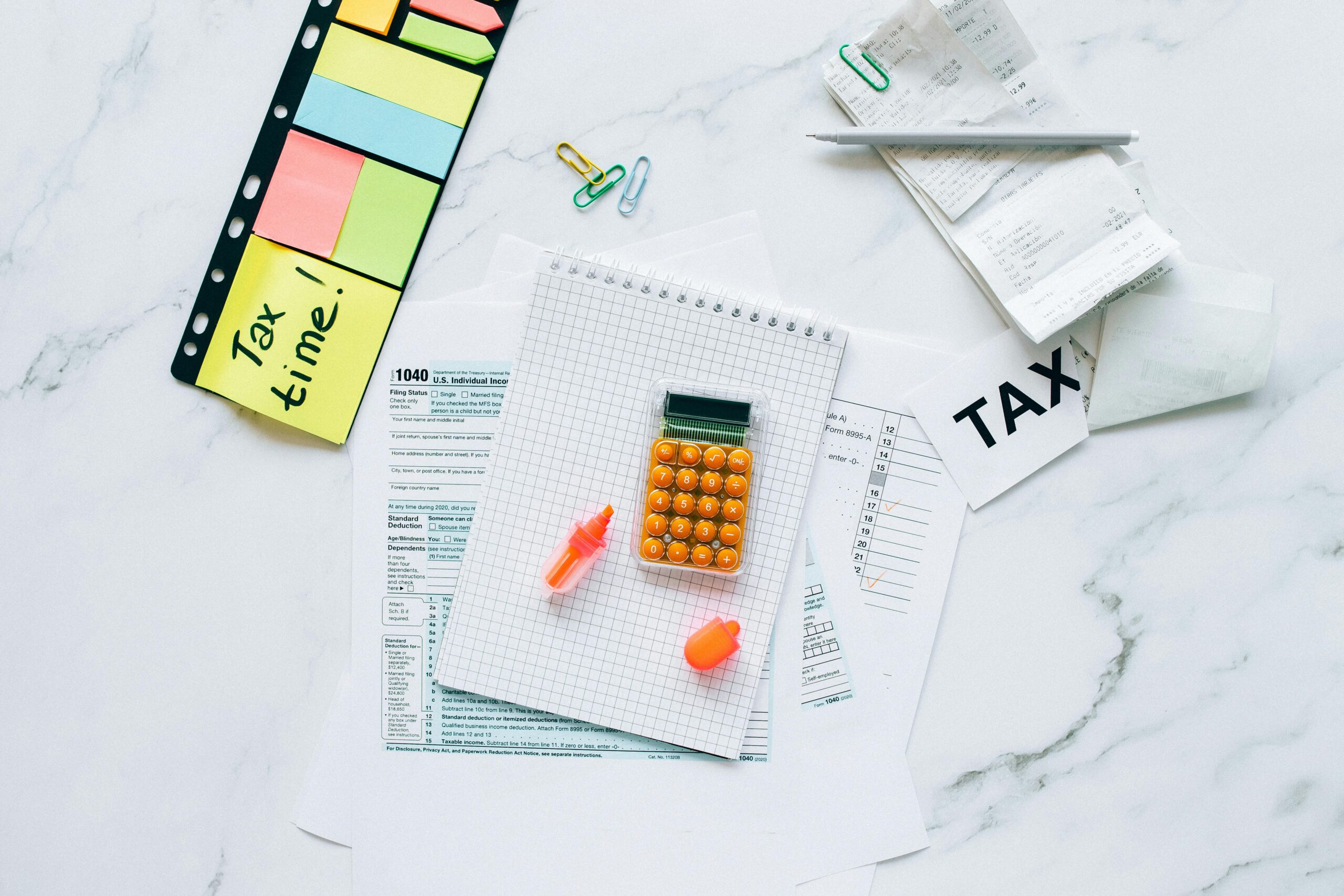 Flat lay of tax preparation essentials with calculator, forms, and colorful sticky notes.